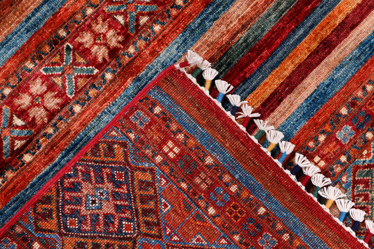 Corner detail of geometric rug with red, blue patterns and white tassel fringe