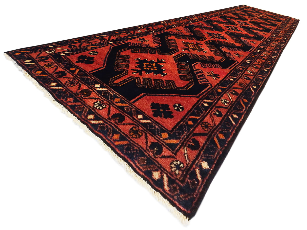 Red and black geometric area rug shown diagonally, with short fringed edges.