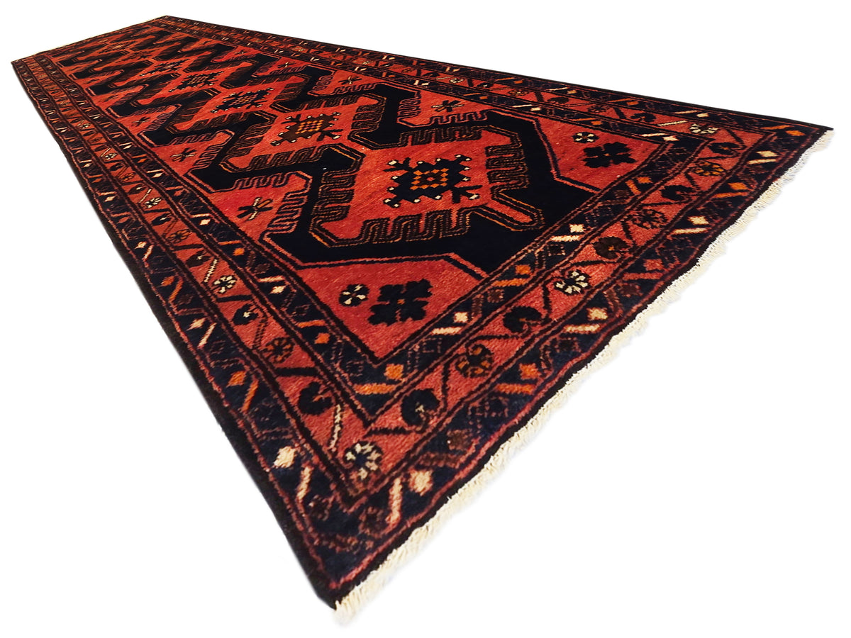Red and black geometric patterned area rug with detailed border and corner motifs.