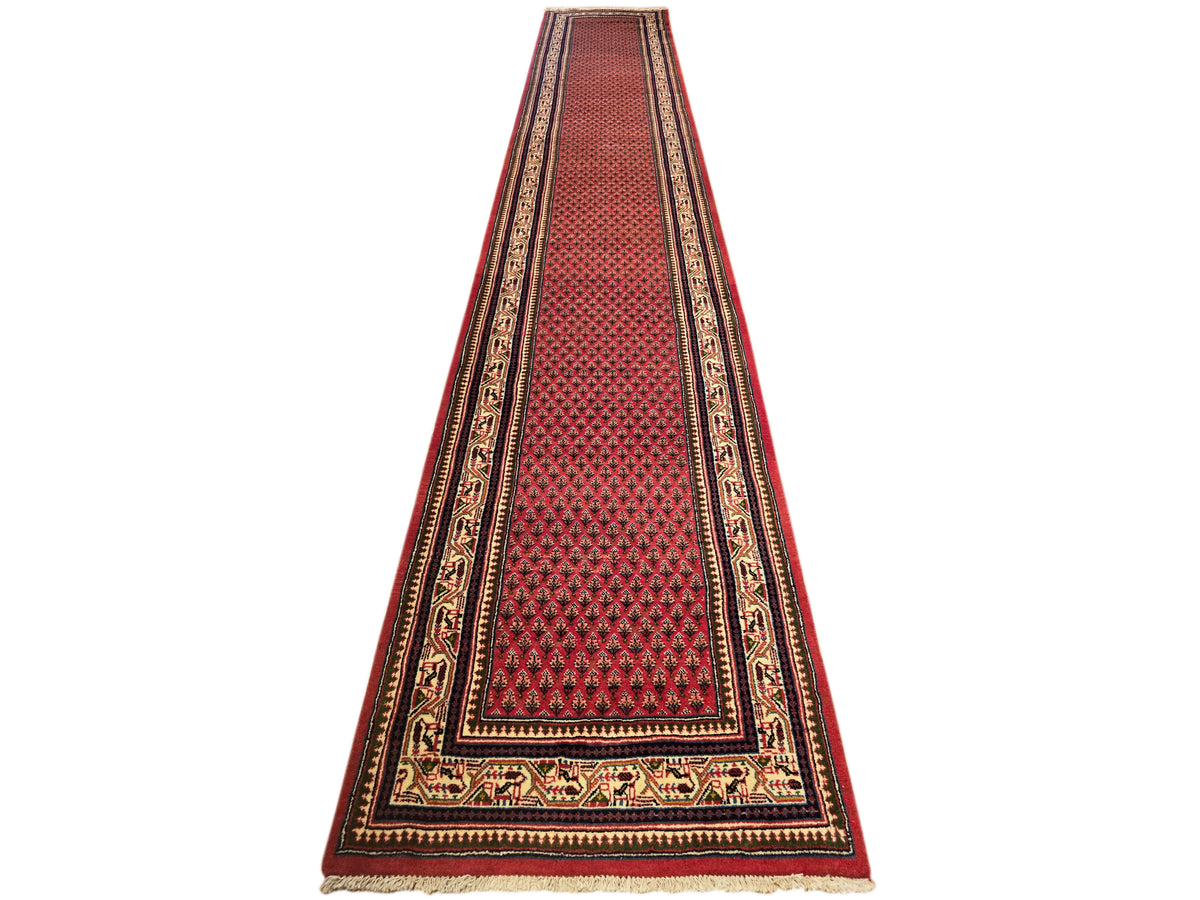 Long red runner rug with repeating diamond texture, dark border, and cream trim