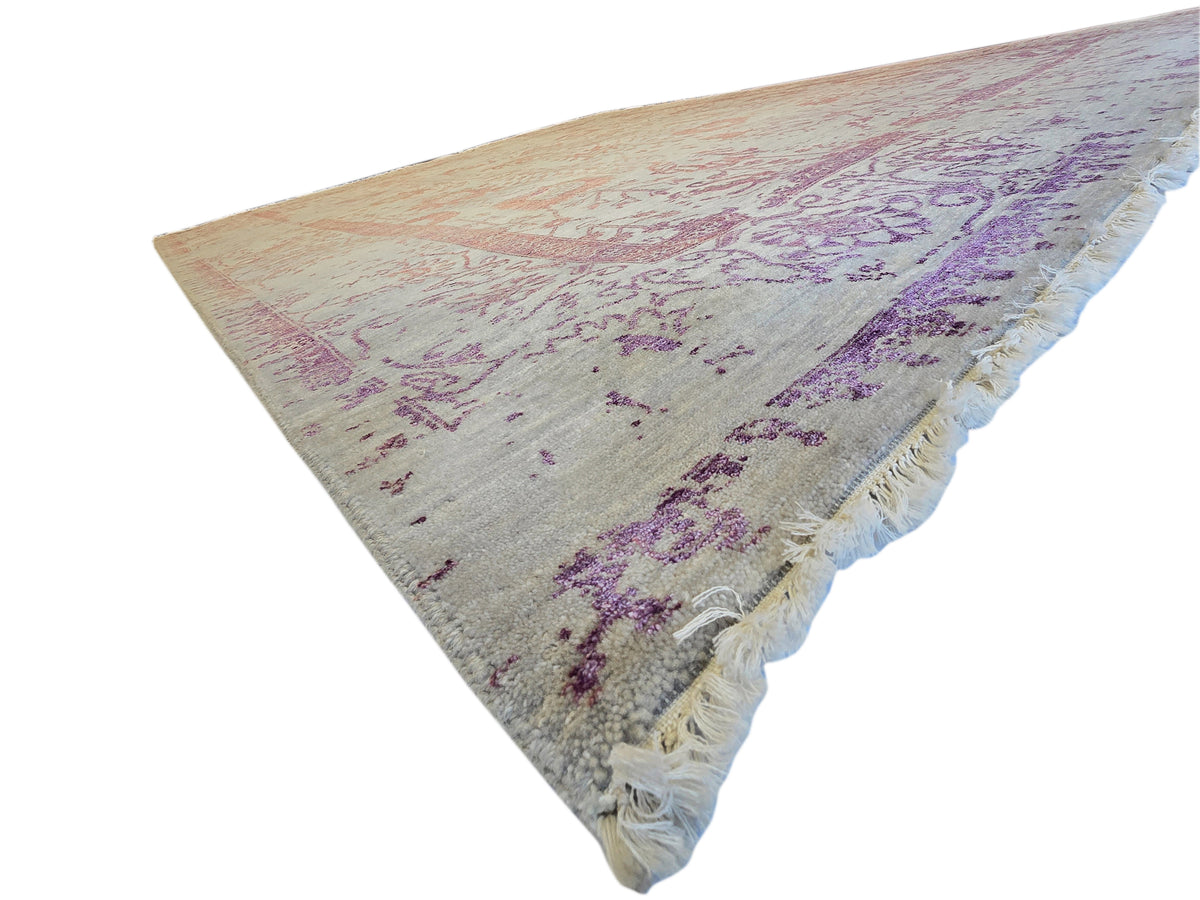 Modern beige area rug with purple pattern and cream fringed corner