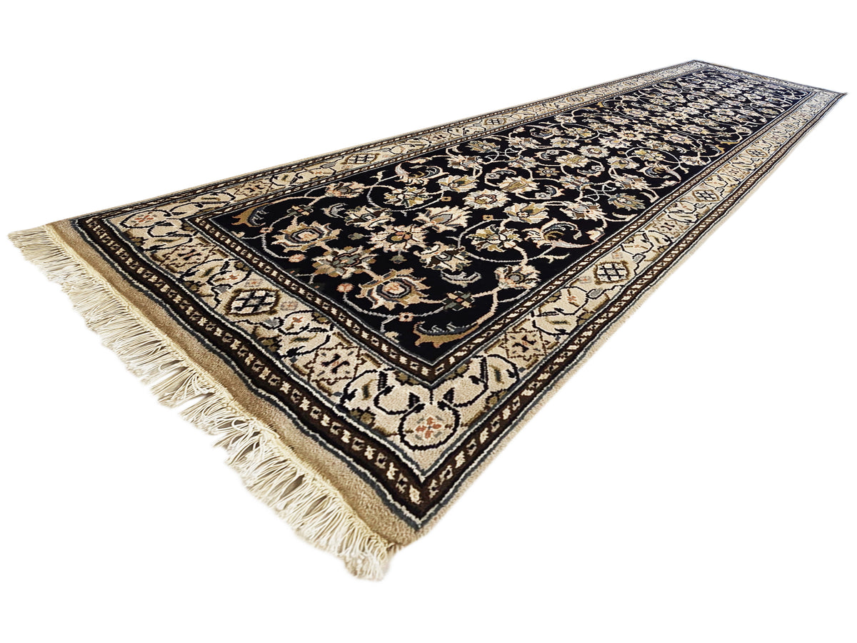 Decorative runner rug corner view with black background, gold accents, and tassel fringe