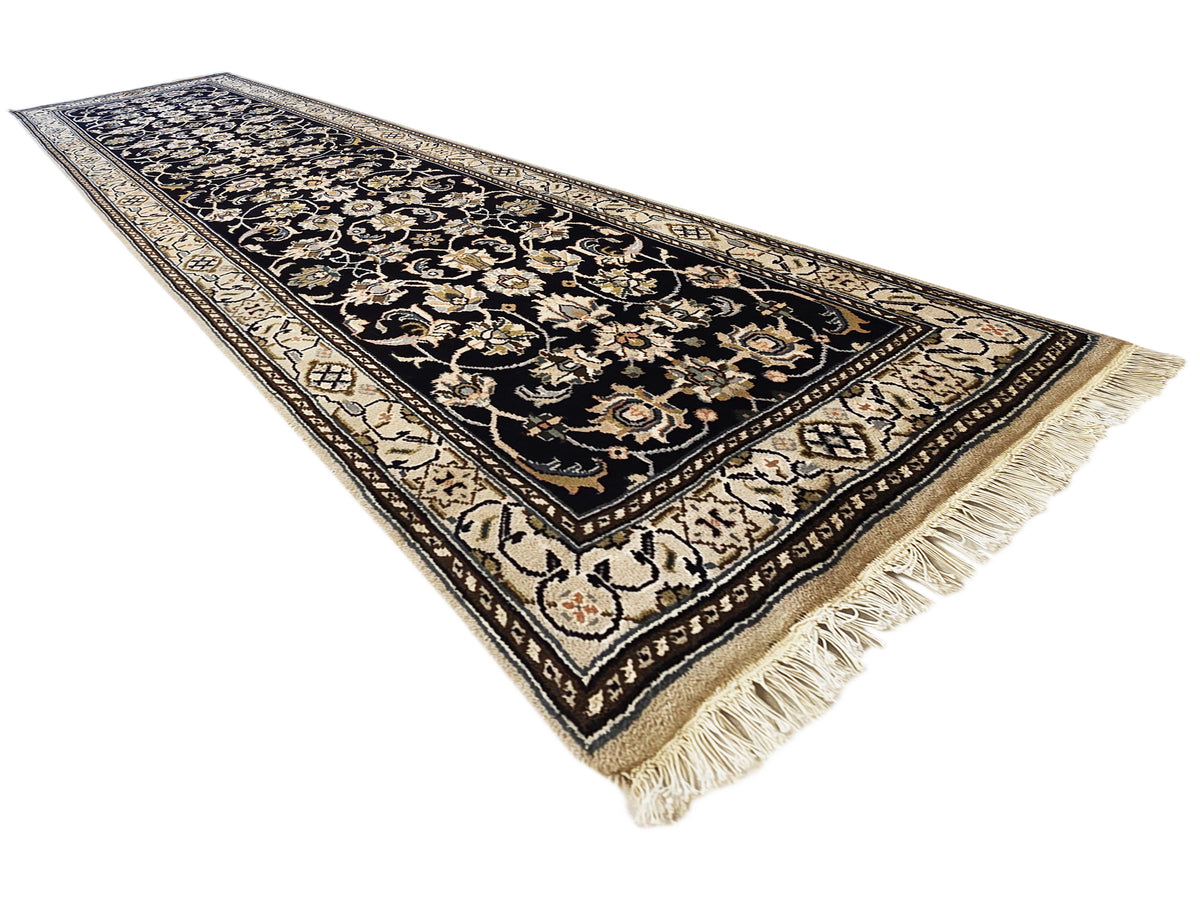 Ornate runner rug at an angle with fringe edges; black, gold, and cream motifs