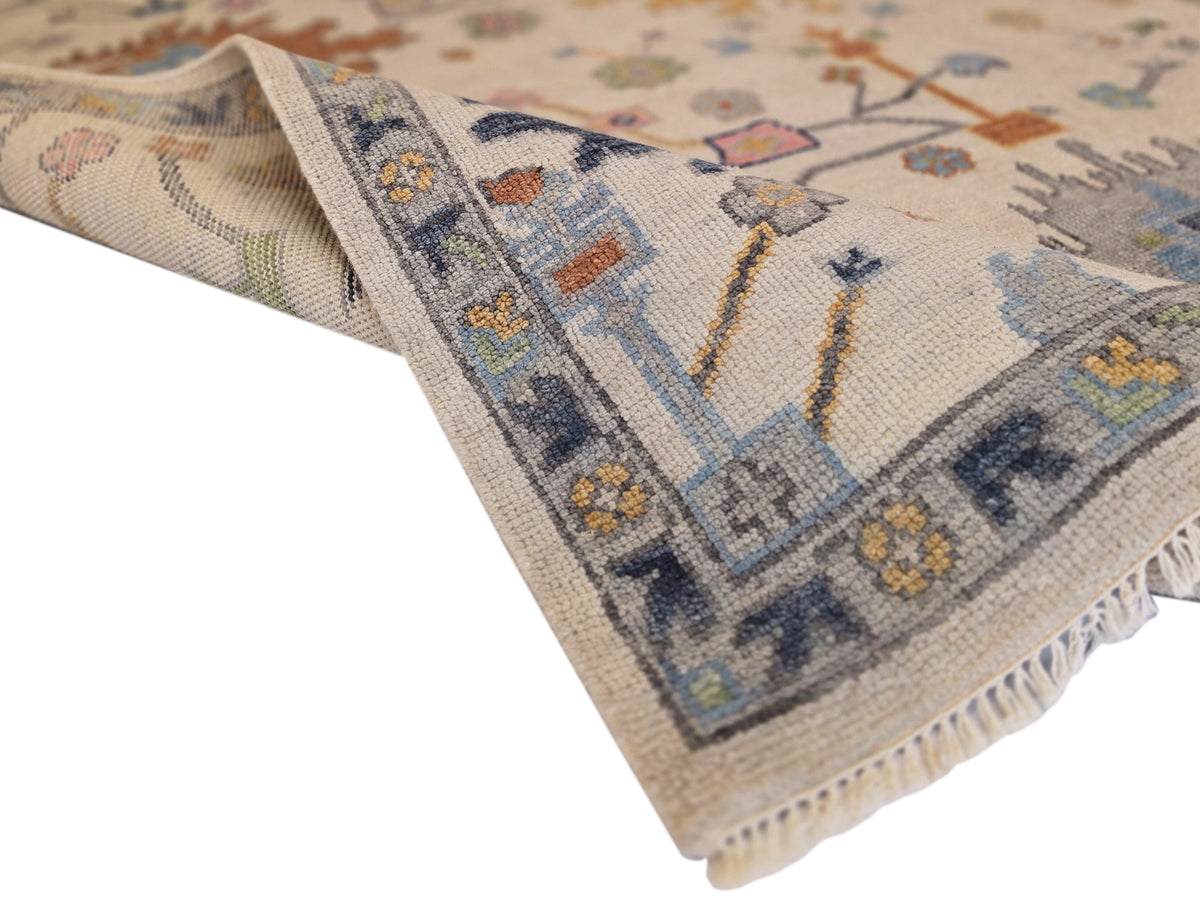 Oushak rug corner detail with fringe, light beige weave, blue border, and multicolor small motifs