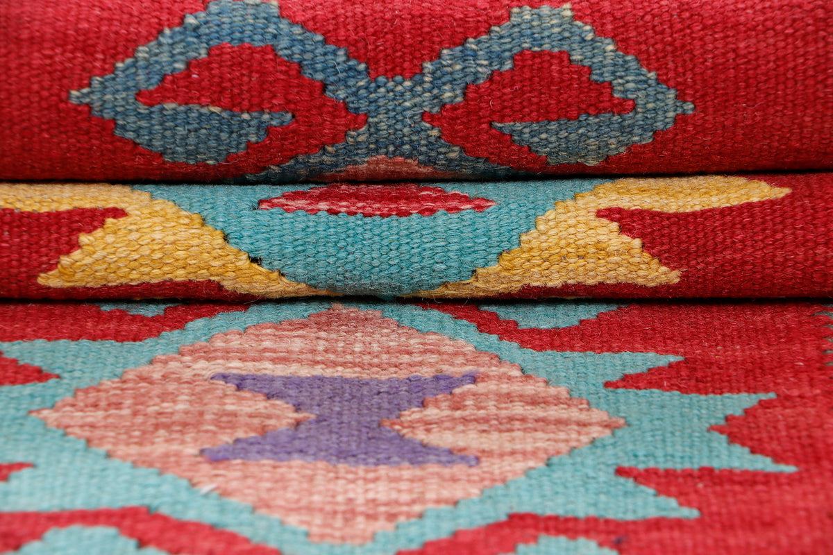 Close-up of kilim rug texture with red ground and teal, blue, beige geometric shapes