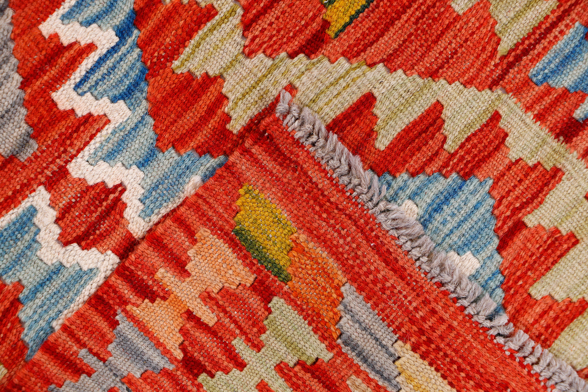 Kilim rug textured weave close-up with red, blue, cream, and green zigzag shapes.