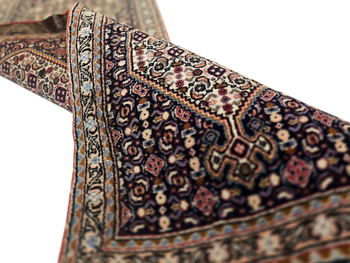 Corner view of dark patterned rug with geometric medallions and multicolor trim fringe