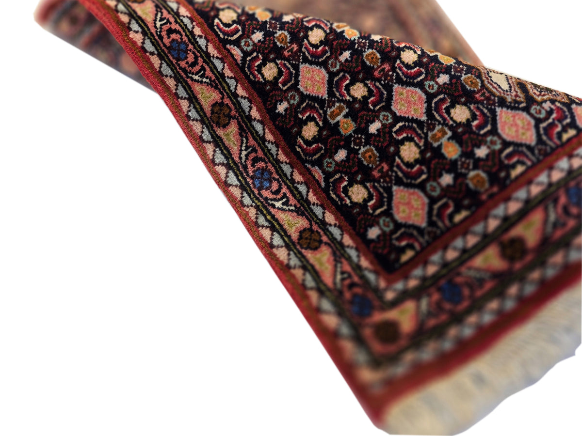 Angled close-up of runner rug pattern with dark base, red border, and soft fringe detail.