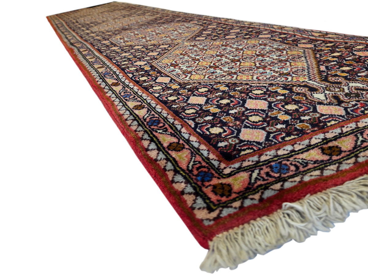Wide angle view of narrow runner rug with dark field, red border, ornate geometric pattern, fringe.