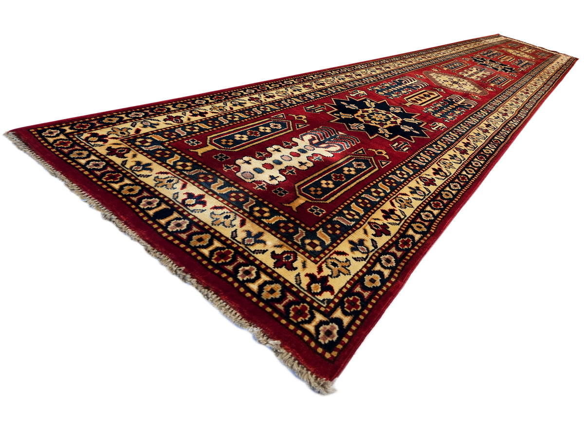 Corner view of rectangular Sherwan rug in red and cream with patterned border and fringes.