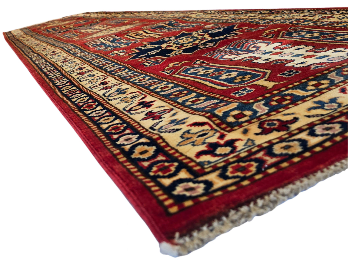 Diagonal Sherwan rug with cream field, navy and red geometric pattern, fringed edge.