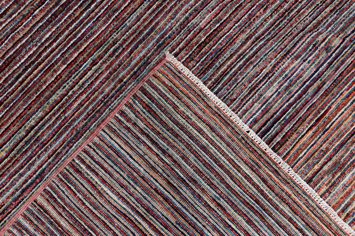 Corner of striped area rug with dark brown base and thin multicolor lines; overstitched edge