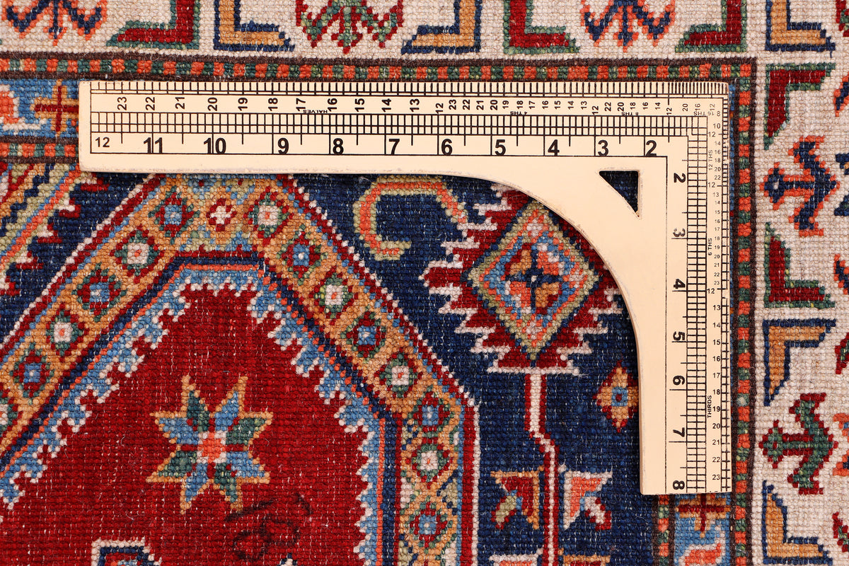 Red and navy patterned rug corner with geometric border and measuring scale