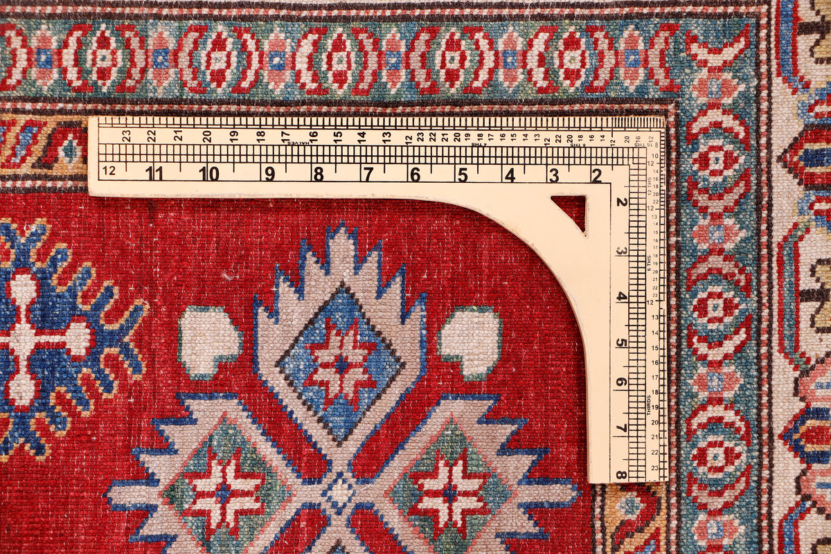 Red rug with diamond centerpiece, blue motifs, and measuring tape on border
