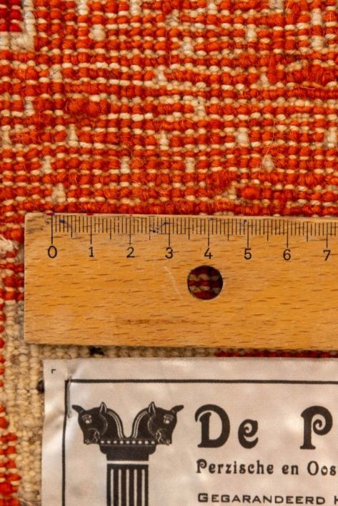 Close-up of a textured orange and beige fabric with a ruler and 'De Pers' label.